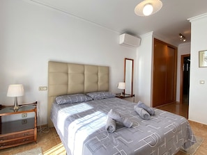 A bedroom with a bed, bedside tables, a lamp, an air conditioning unit, and a mirror. - Apartment in Nerja Near Carabeo Beach (Nerja)