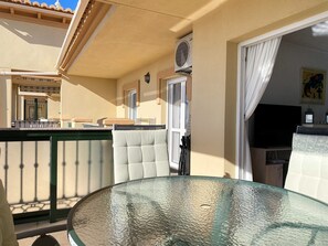 A glass-top table with a cushioned chair, a balcony with a railing, and a door with curtains. - Apartment in Nerja Near Carabeo Beach (Nerja)