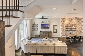 A spacious living area with a sofa, television, and a brick wall. - Rooftop EaDo Nr Downtown | Yard BBQ Games WiFi (Houston)