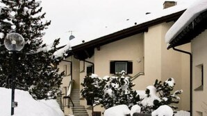 A snow-covered outdoor area with a building, a staircase, and snow-covered trees. - Apartment  by Interhome (Celerina)