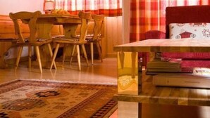 A room with a wooden dining table, chairs, a patterned rug, and a sofa with a red throw. - Apartment  by Interhome (Celerina)
