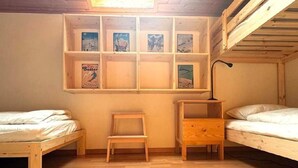A room with two bunk beds, a small wooden chair, and a shelf with framed pictures. - Apartment  by Interhome (Celerina)