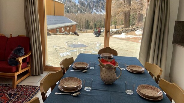 Ein Essbereich mit einem Tisch für sechs Personen, einem roten Sofa und Blick auf eine Hütte und einen Wald.