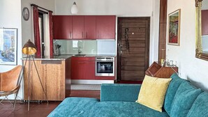 A modern living room with a teal sofa, a wooden coffee table with fruit, a pendant light, and a kitchen in the background. - Residenza Viramonte - Casa Bianca, Wohnung 14 by Interhome (Vira)