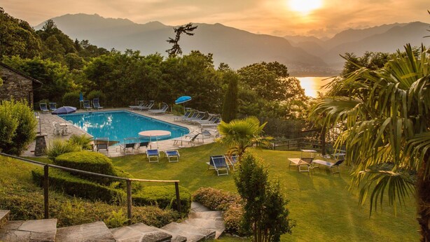 Une piscine entourée de chaises longues et de parasols, avec une végétation luxuriante et des montagnes en toile de fond.