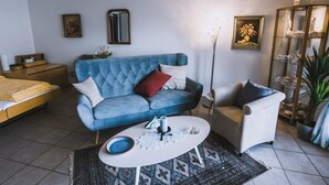 Un salon avec un canapé bleu, un fauteuil blanc, une petite table basse et une vitrine contenant des objets décoratifs.
