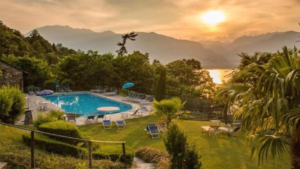 A pool area with lounge chairs and umbrellas, surrounded by greenery and mountains in the background. - Residenza Viramonte - Casa Cecilia, Wohnung 24 by Interhome (Vira)
