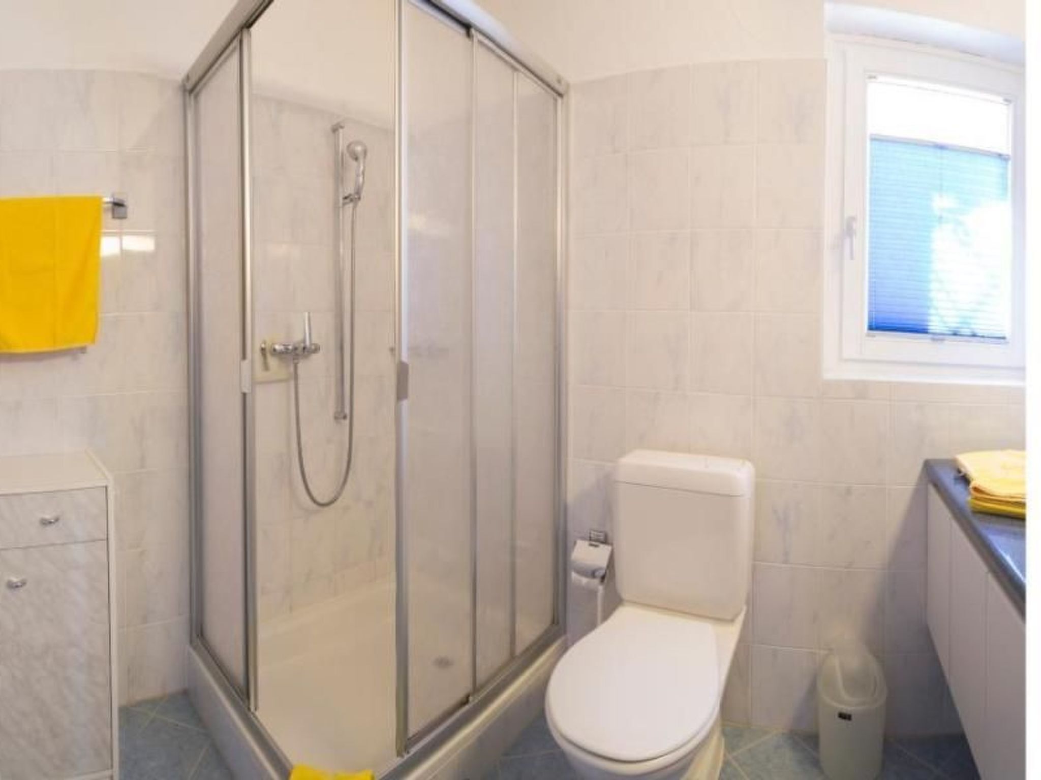 Un baño con ducha de vidrio, inodoro y un pequeño armario.
