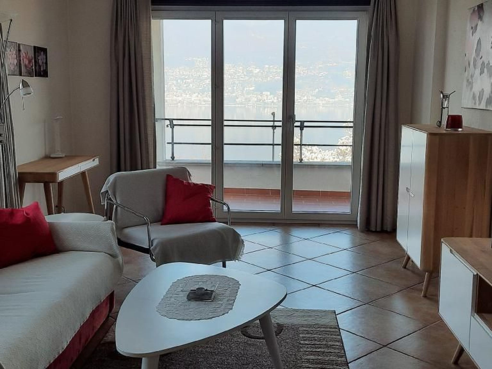 Un salon moderne avec un canapé, un fauteuil et une table basse. Une grande porte-fenêtre coulissante donne accès à un balcon offrant une vue sur la ville.