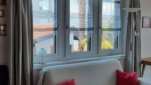 Una habitación con sofá, ventana con cortinas y lámpara.
