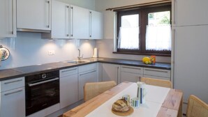 Eine moderne Küche mit weißen Schränken, einem eingebauten Backofen und einem Essbereich mit einem Holztisch und Korbstühlen.