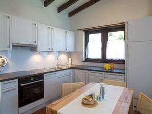 Eine moderne Küche mit weißen Schränken, einem eingebauten Backofen und einem Essbereich mit einem Holztisch und Korbstühlen.