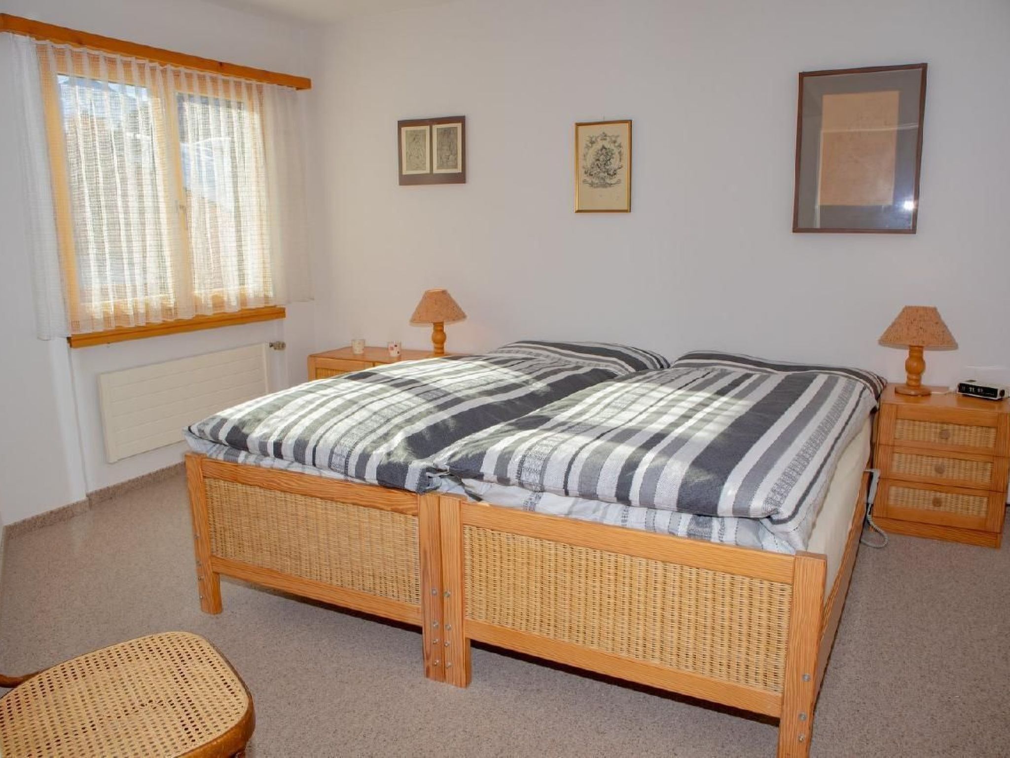 Ein Schlafzimmer mit einem hölzernen Bett, zwei Nachttischen, einem Korbstuhl und einem Fenster mit Vorhängen.