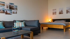 Una sala de estar moderna con un sofá gris, una mesa de centro de madera, una cama con estructura de madera y una alfombra.