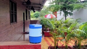 A covered outdoor area with a water dispenser, potted plants, and a red umbrella. - MARS Resort (Shahapur)