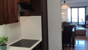 A modern kitchen with dark wooden cabinets, a white countertop, and a black stove. There is a small potted plant on the counter. The kitchen leads to a dining area with a table and chairs. - Residenza Viramonte - Casa Aurelia, Wohnung 8 by Interhome (Vira)