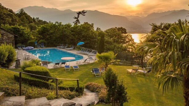 A pool area with lounge chairs and umbrellas, surrounded by lush greenery and mountains in the background. - Residenza Viramonte - Casa Aurelia, Wohnung 8 by Interhome (Vira)