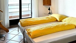 Una camera da letto con due letti, un armadietto in legno, un tavolino con una lampada e vista all'esterno da una grande finestra.
