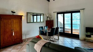 Un soggiorno con divano, tavolo da pranzo con sedie, un armadietto in legno e un'ampia finestra vista mare.