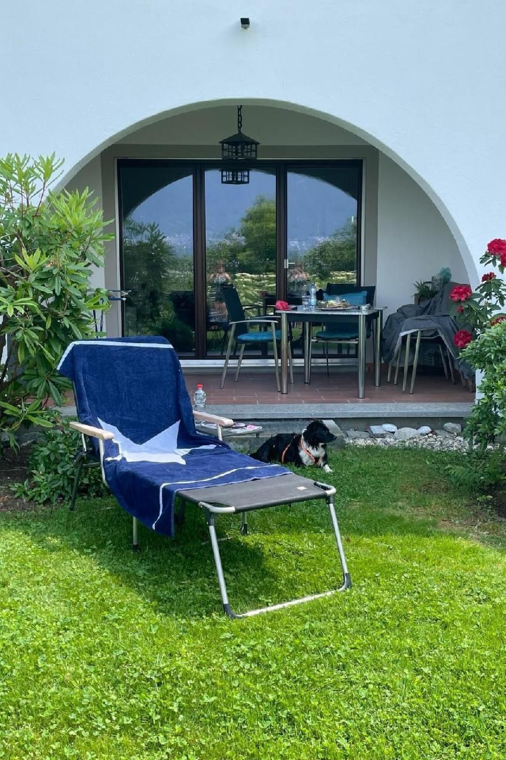 Ein überdachter Sitzbereich im Freien mit Tisch, Stühlen und einer Liege, außerdem ein Hund.