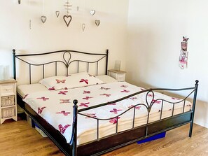 A bedroom with a metal-framed bed, white bedding with pink butterfly prints, a bedside table with a lamp, and a wall decoration of hearts and a butterfly. - Residenza Viramonte - Casa Daniela, Wohnung 31 by Interhome (Vira)