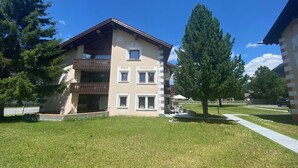 A multi-story building with a balcony, a lawn in front, and trees. - Sassella 2a by Interhome (La Punt-Chamues-ch)