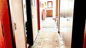 A hallway with a patterned rug, a kitchen area in the background, and a door with a brass handle. - Sassella 2a by Interhome (La Punt-Chamues-ch)