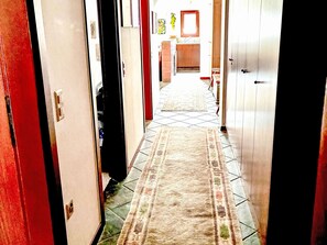 Un pasillo con un tapete estampado, una zona de cocina al fondo y una puerta con picaporte de latón.