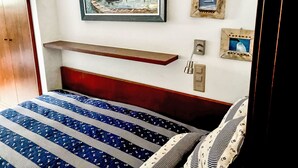 A bedroom with a bed, a painting, a shelf, and a wall-mounted light fixture. - Sassella 2a by Interhome (La Punt-Chamues-ch)