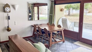 A dining area with a wooden table and chairs, a clock on the wall, and a view through a glass door. - Sassella 2a by Interhome (La Punt-Chamues-ch)