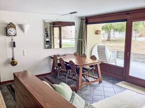 Un comedor con una mesa y sillas de madera, un reloj en la pared y vistas a través de un ventanal.