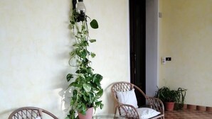 Una terrazza con sedie in vimini e un tavolo in vetro, circondata da piante in vaso e un pavimento piastrellato.