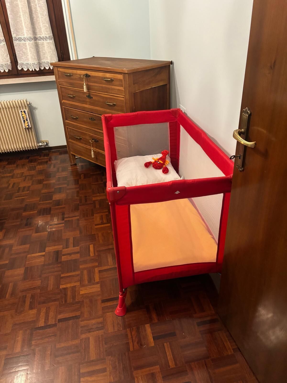 Une pièce avec un berceau rouge, une commode en bois et un parquet.