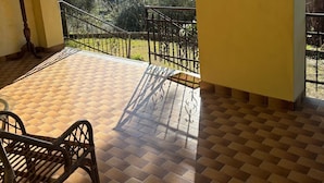 Un balcone con pavimento in piastrelle, ringhiera in ferro battuto e vista su una collina.