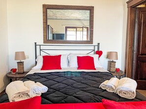 Una cama bien hecha con almohadas rojas y blancas, una colcha negra y toallas enrolladas al lado.