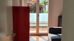 A room with a sliding glass door leading to a balcony, a red door, and a black sofa. - Haus in Agno by Interhome (Agno)