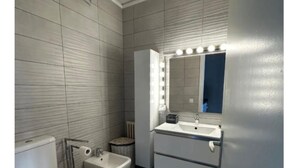 A modern bathroom with a toilet, bidet, vanity with a mirror and lights, and a radiator. - Paradise Lake View by Interhome (Lugano)