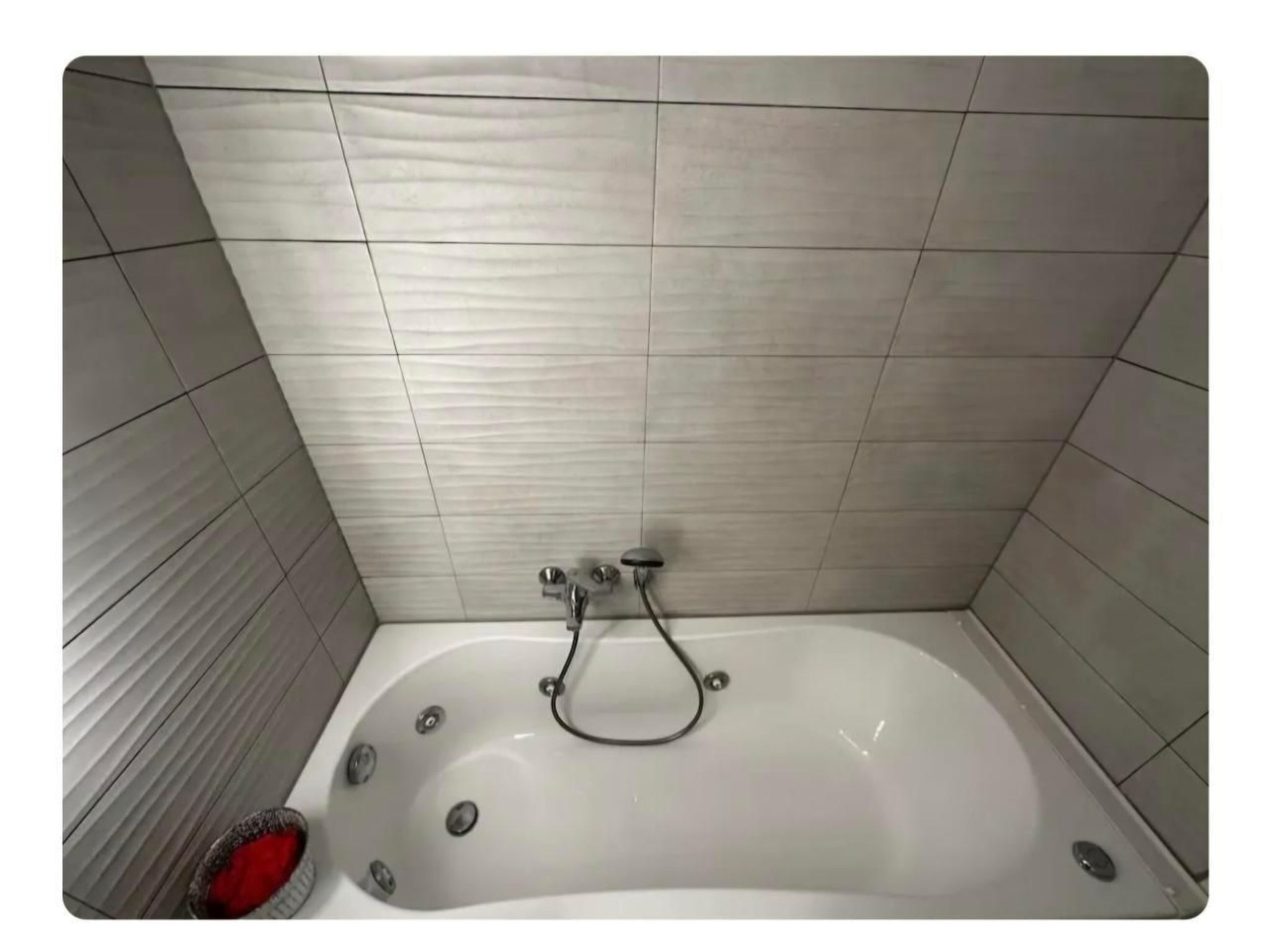 A bathroom with a white bathtub, tiled walls, and a red bath mat.