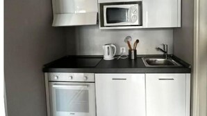A compact kitchen with white cabinets, a microwave, a stove, and a sink. - Paradise Lake View by Interhome (Lugano)