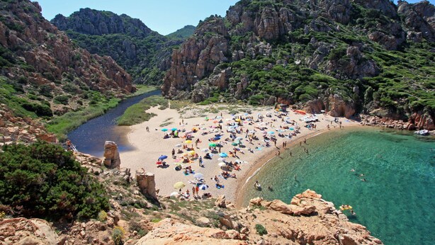 Ein Küstenstrand mit felsigen Klippen und klarem, türkisblauem Wasser.