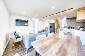 A modern kitchen with a wooden dining table, grey sofas, and a large vase with pampas grass. - Cosy & Contemporary Airport Retreat (Papatoetoe Auckland)