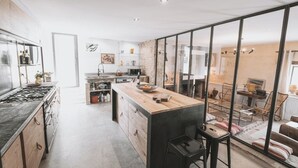 A modern kitchen with a central island, wooden cabinets, and a large window overlooking the dining area. - Gîte in the heart of the vineyards (Larroque)