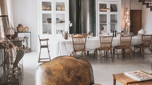 A dining area with a white table set for six, surrounded by wicker chairs. A black column and a staircase are visible in the background. - Gîte in the heart of the vineyards (Larroque)