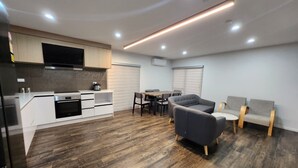 A modern kitchen with white cabinetry, a built-in oven, and a flat-screen TV. - Cosy & Contemporary Airport Retreat (Papatoetoe Auckland)
