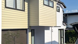 A two-story house with a garage, a driveway, and a small garden area with plants and gravel. - Cosy & Contemporary Airport Retreat (Papatoetoe Auckland)