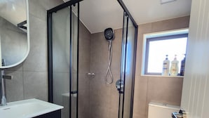 A modern bathroom with a glass-enclosed shower, a white toilet, and a black vanity with a mirror. - Cosy & Contemporary Airport Retreat (Papatoetoe Auckland)