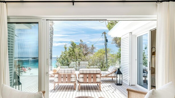 Un ampio balcone con pavimento in legno, sedute imbottite bianche e vista sull'oceano.