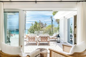 Een ruim balkon met houten vloeren, witte, beklede zitplaatsen en uitzicht op zee.