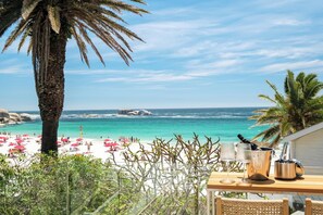 Eine Terrasse am Strand mit Blick auf den Ozean, Palmen und einem Tisch mit Getränken und Gläsern.
