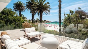 Una terrazza con poltrone e pouf che si affaccia su una spiaggia con palme e cielo sereno.